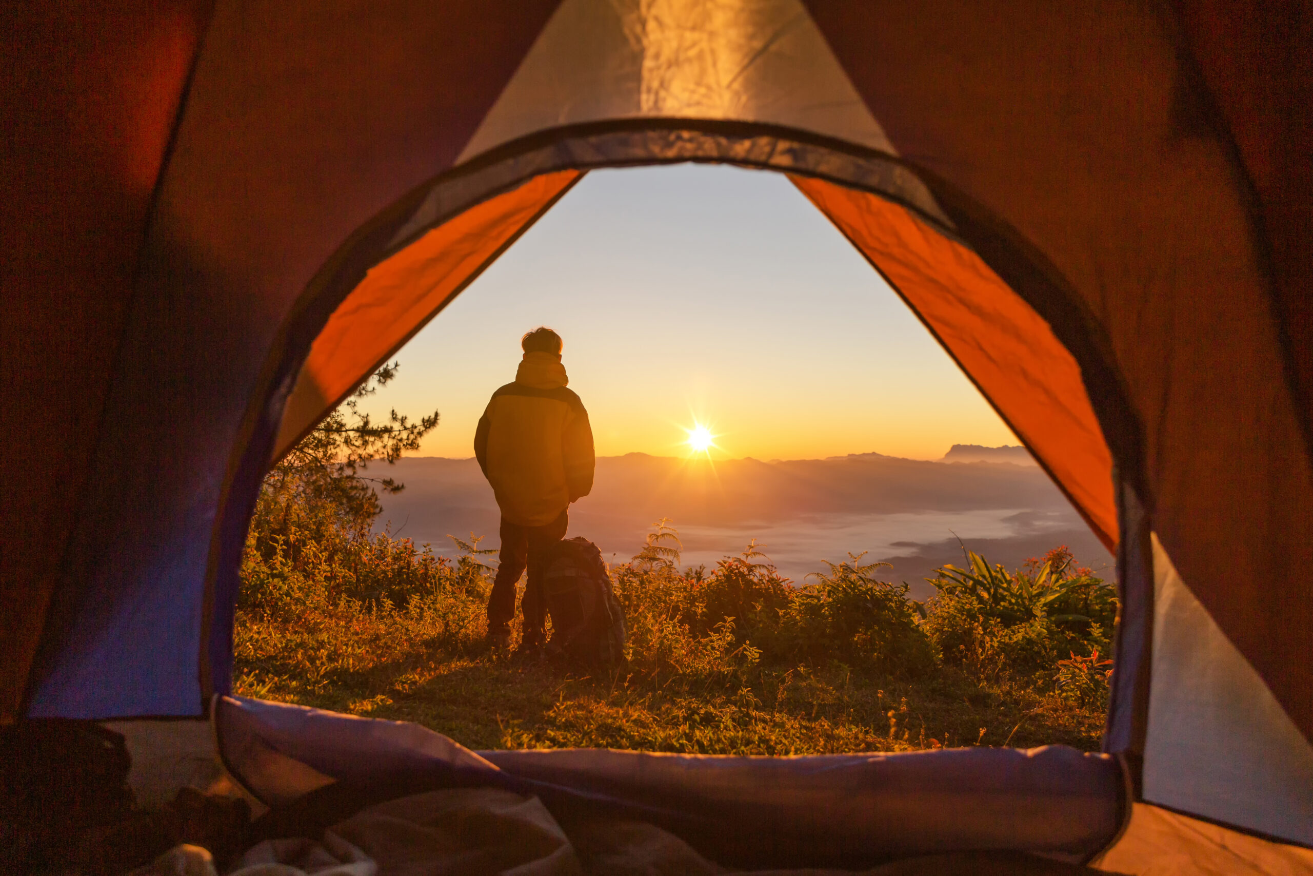 Hiker stand at the camping near orange tent and backpack in the