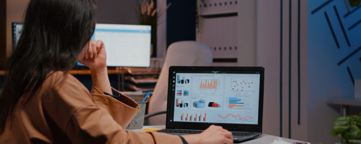 Overworked businesswoman typing financial statistics on laptop sitting at desk